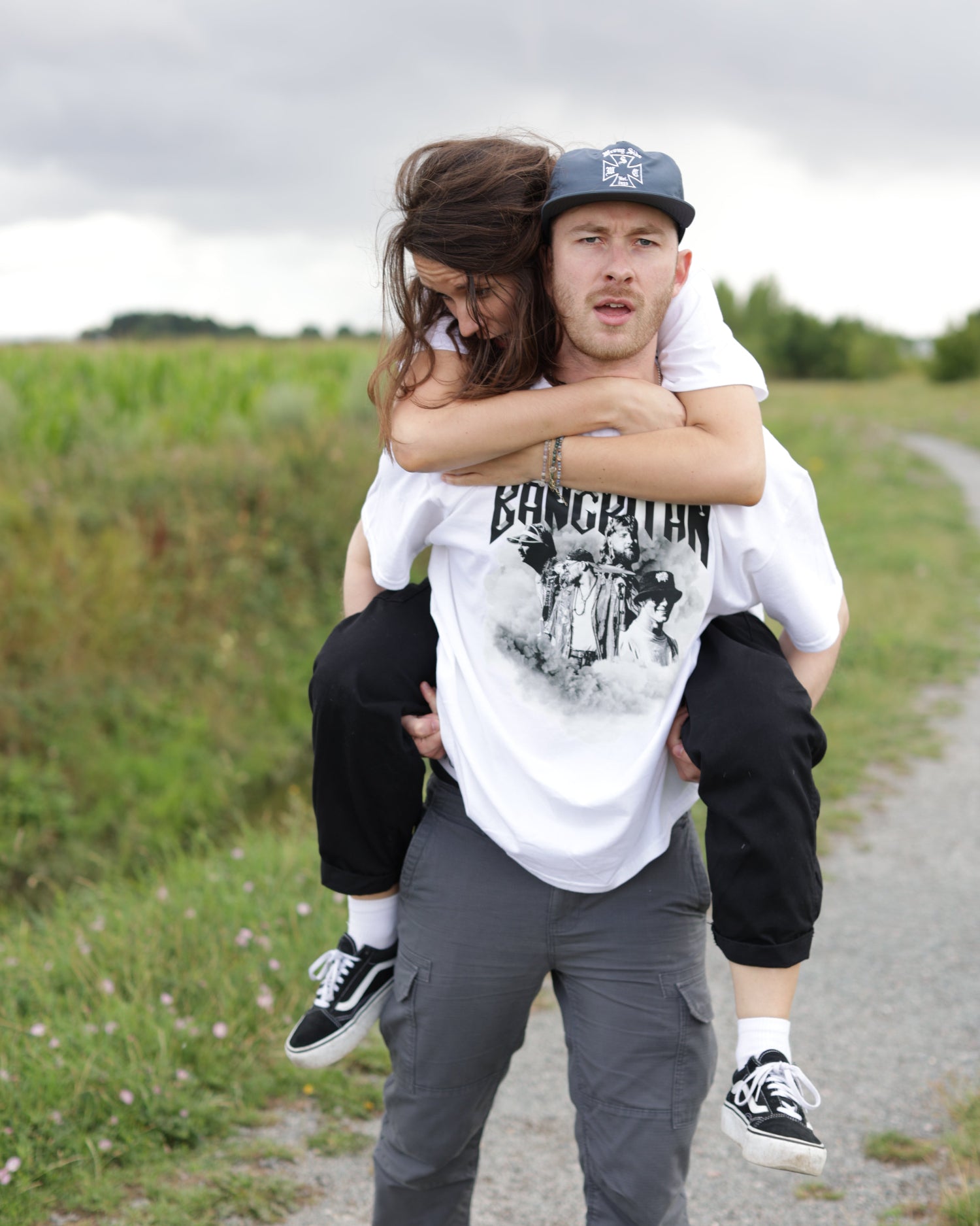 Two people wearing white BANGKITAN t-shirts embracing on a road with grass in the background
