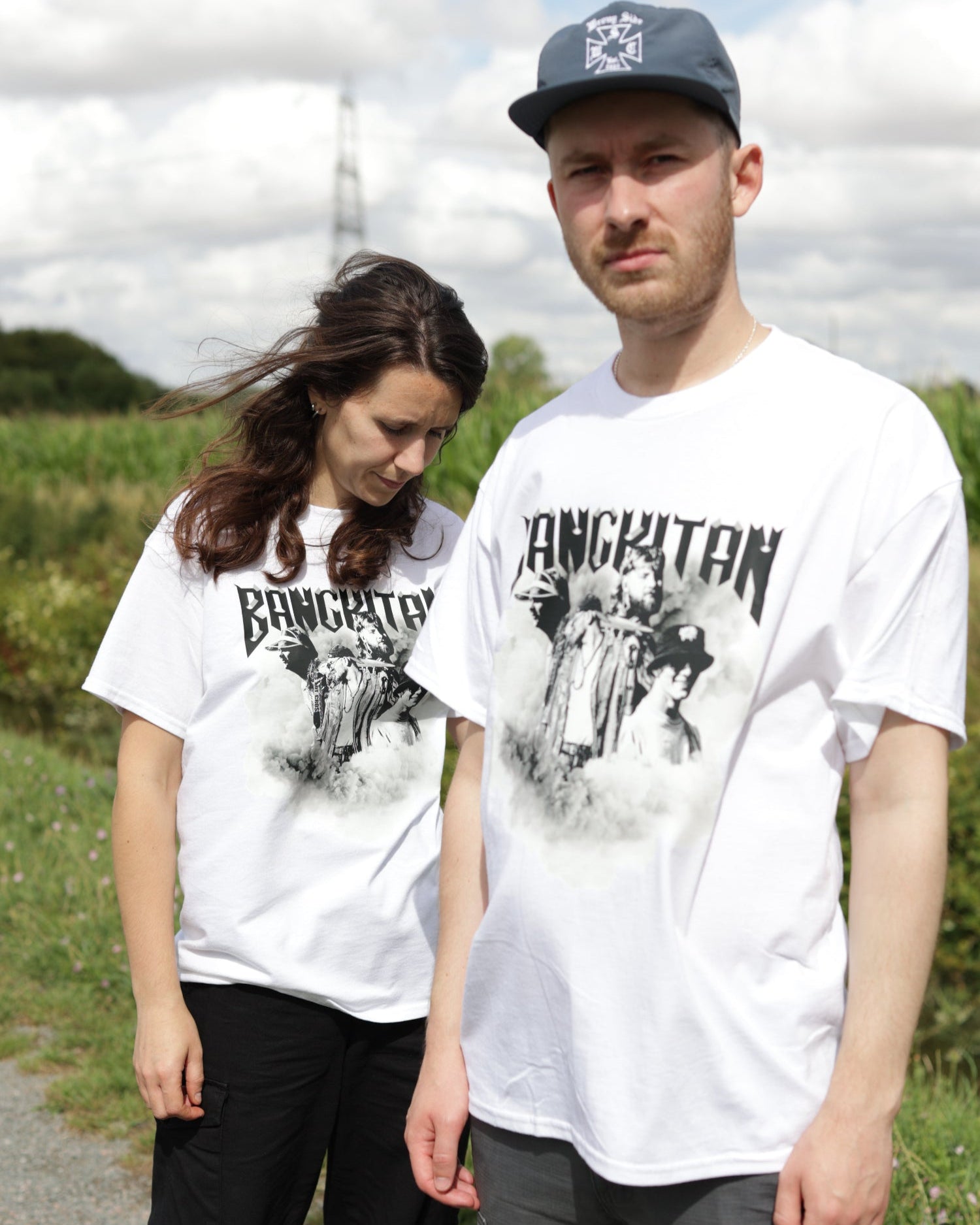 Two people wearing white BANGKITAN t-shirts outdoors with a cloudy sky.