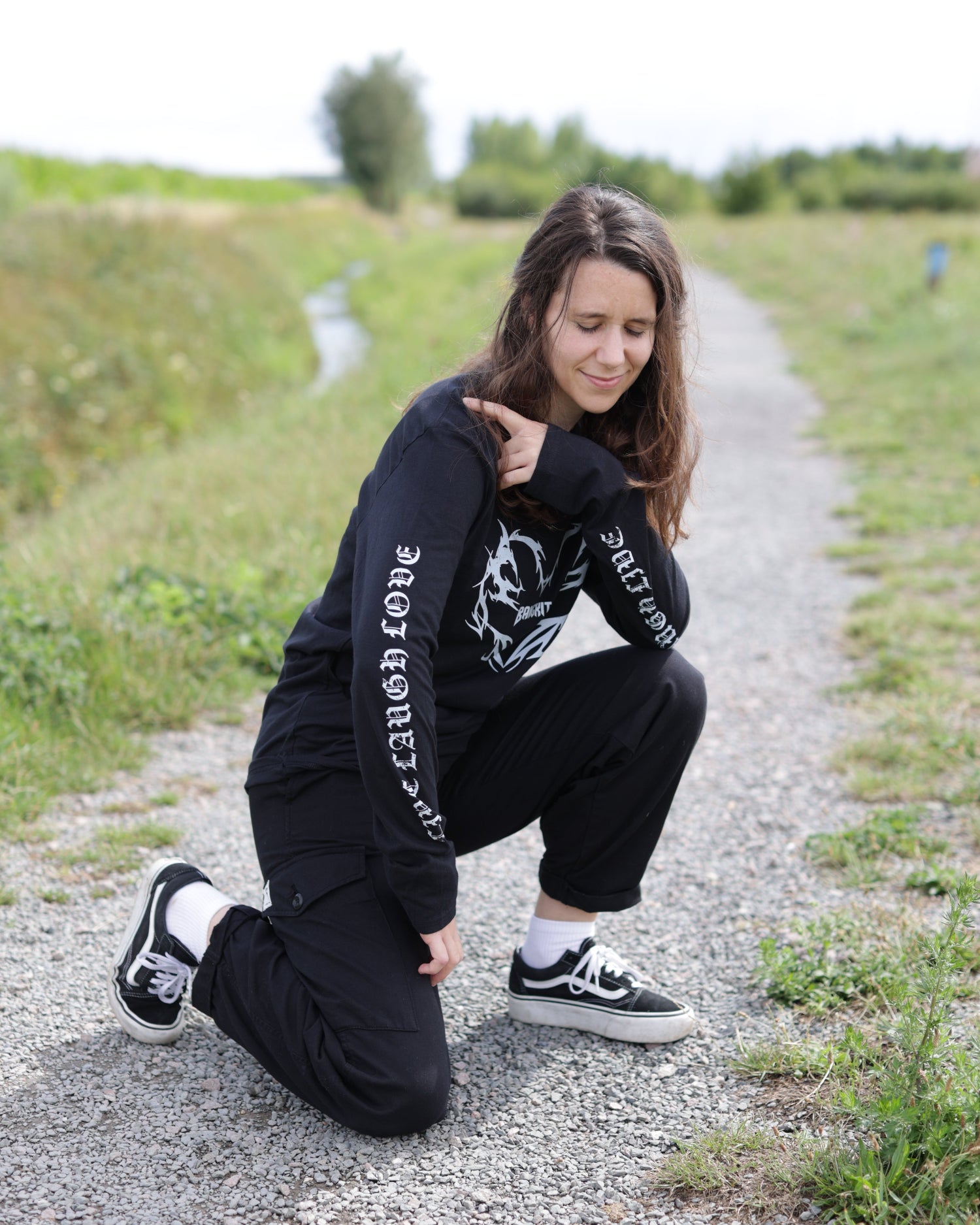 Person wearing a black BANGKITAN long-sleeved t-shirt with text, sitting on a gravel path.