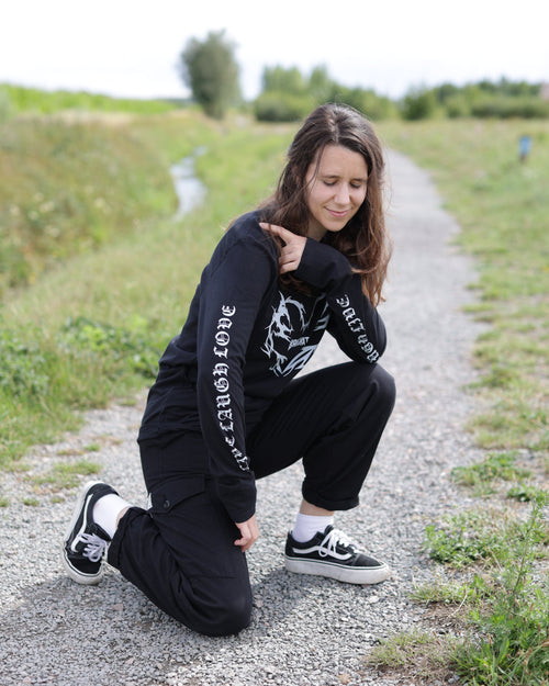 Person wearing a black BANGKITAN long-sleeved t-shirt with text, sitting on a gravel path.