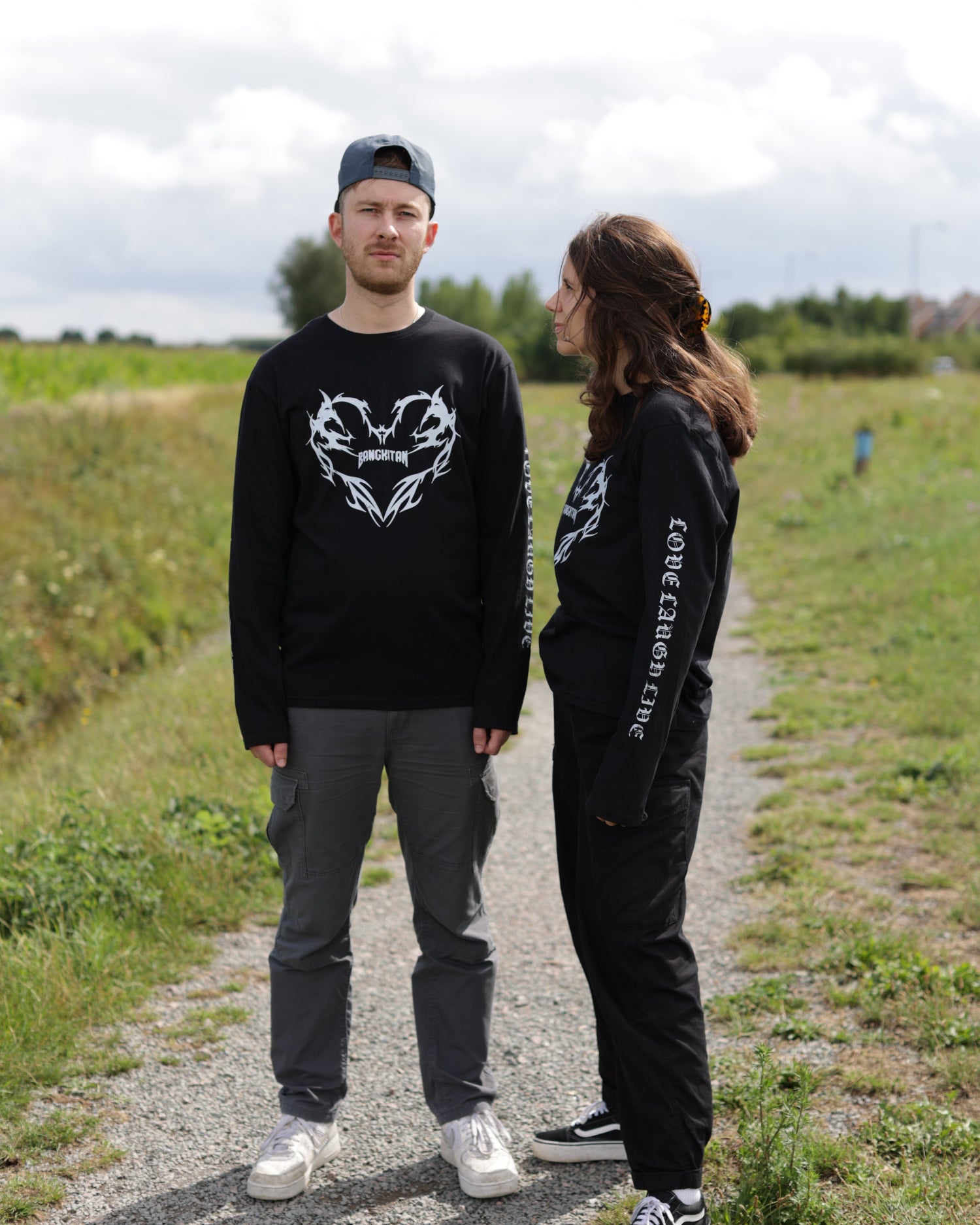 Two people wearing black long-sleeved BANGKITAN t-shirts with white graphics outdoors on a path.