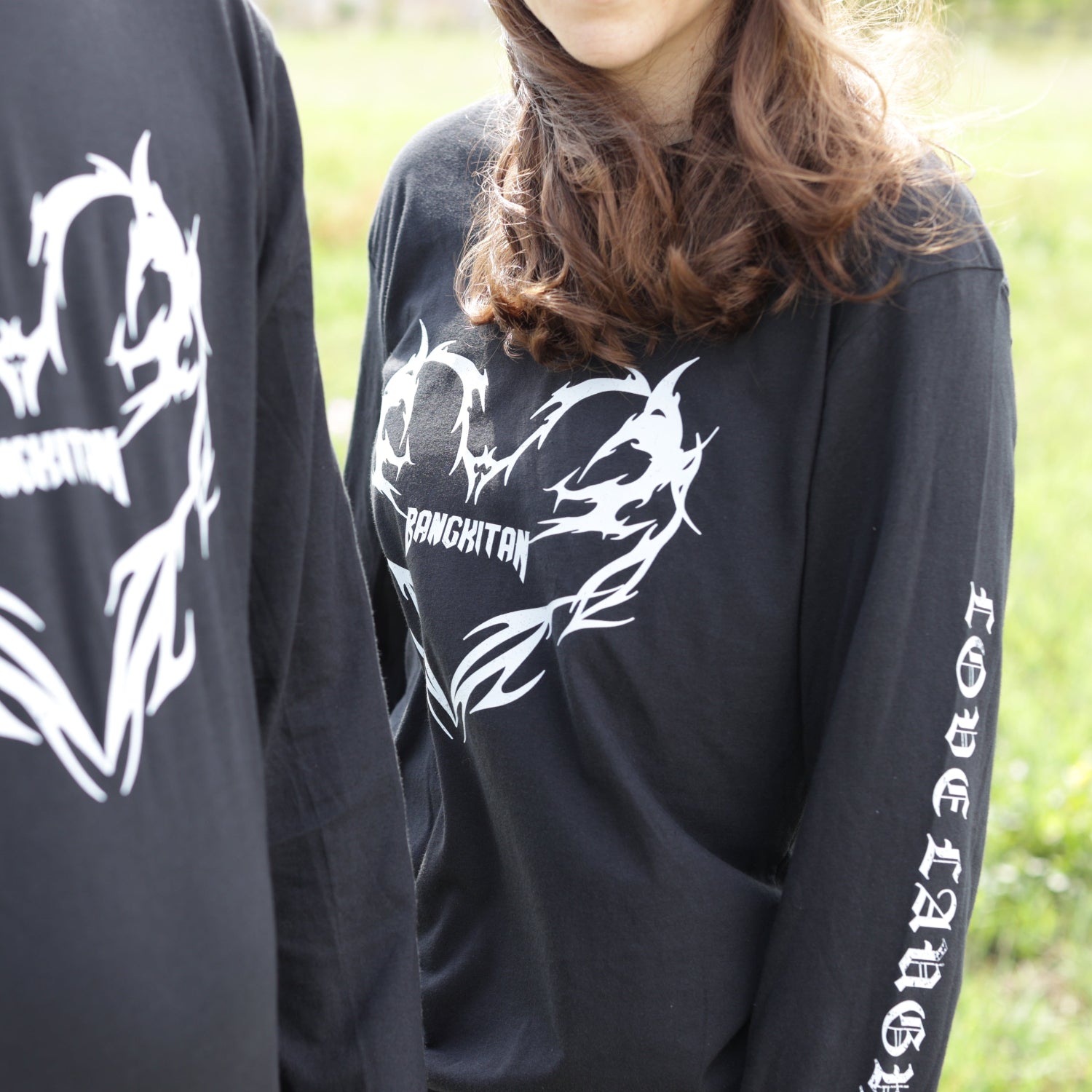 Two people wearing black long-sleeve BANGKITAN shirts with white designs outdoors.