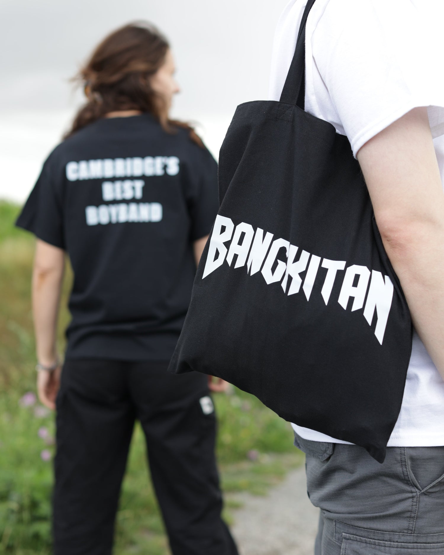 Two people holding BANGKITAN tote bags outside.
