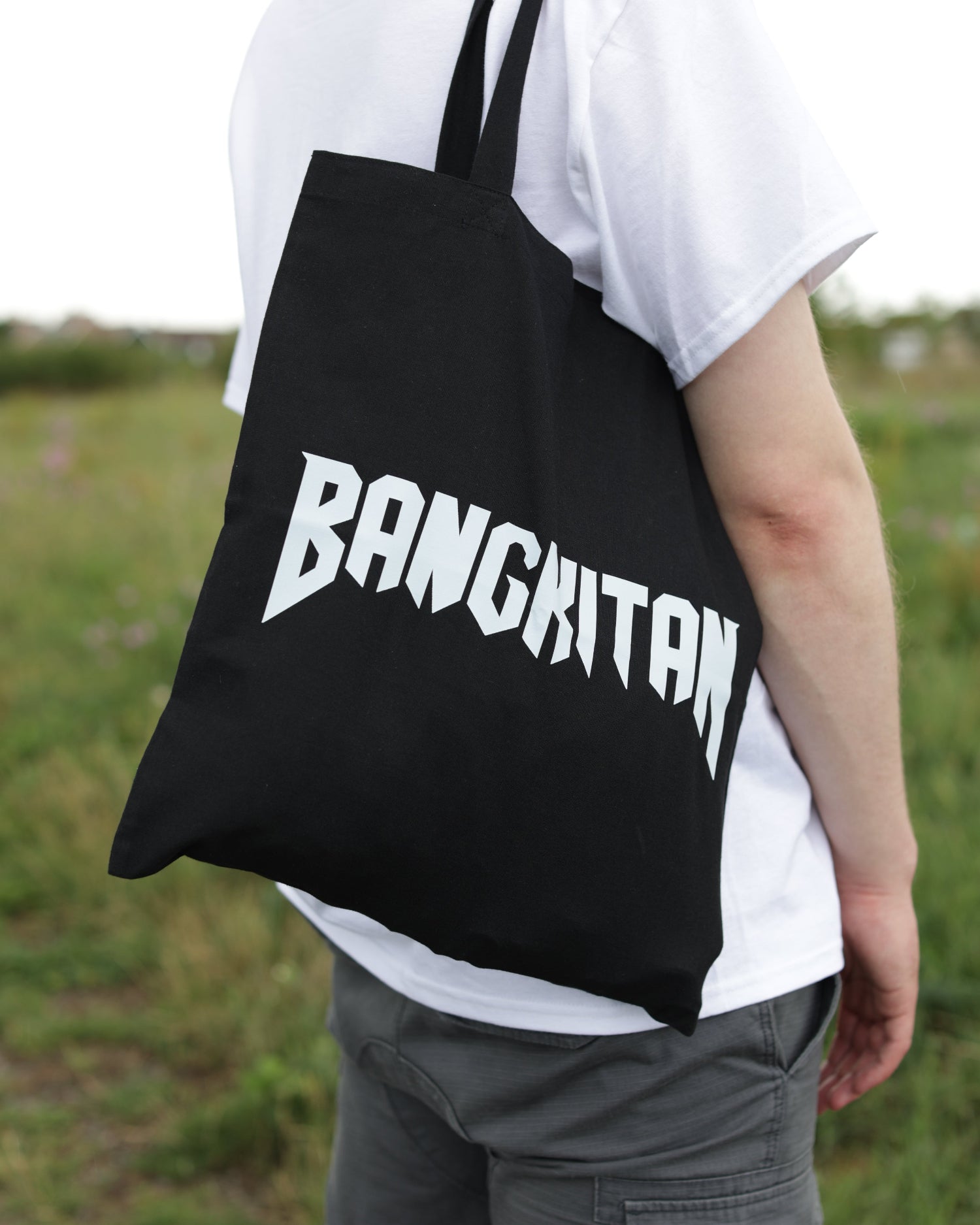 Person holding a black drawstring bag with BANGKITAN printed on it against a blurred green background.